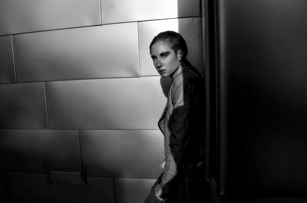 Ett svartvitt foto av en kvinna som står i ett ljusbelyst hörn av ett dunkelt rum.
